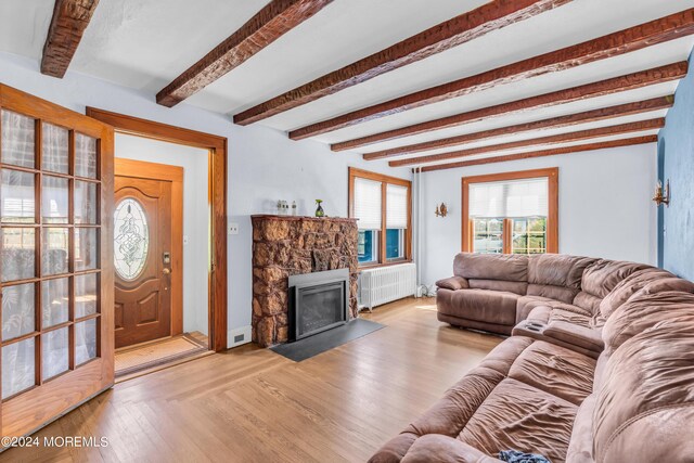 living room with light wood-type flooring, a stone fireplace, beamed ceiling, and radiator