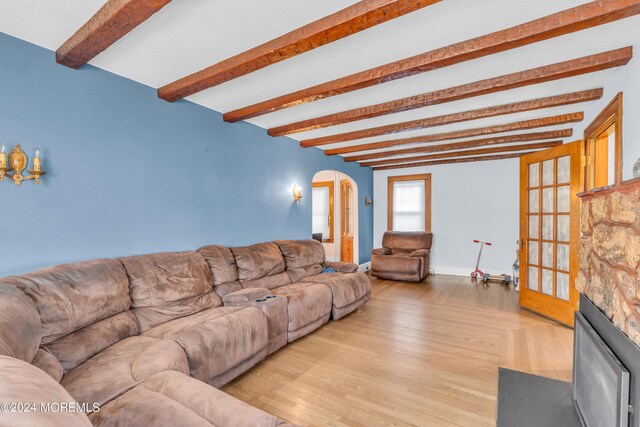 living room with beamed ceiling, a stone fireplace, and light wood-type flooring