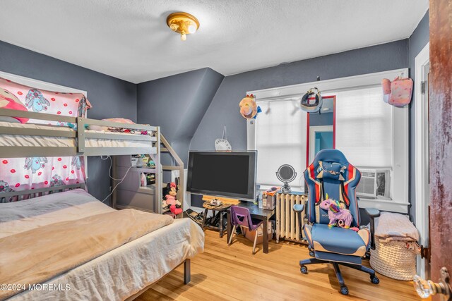 bedroom featuring hardwood / wood-style flooring, a textured ceiling, radiator heating unit, and cooling unit