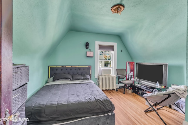 bedroom with cooling unit, light wood-type flooring, a textured ceiling, radiator, and vaulted ceiling