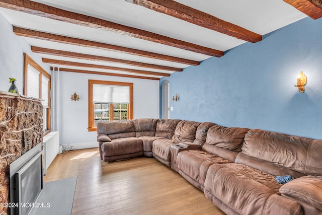 living room with a stone fireplace, beamed ceiling, and light wood-type flooring