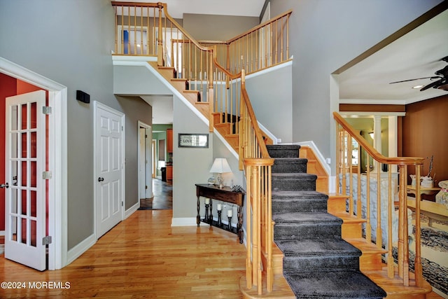 staircase with ceiling fan, crown molding, a high ceiling, and wood-type flooring