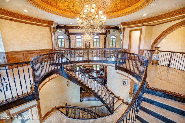 stairs featuring crown molding, an inviting chandelier, a raised ceiling, and a towering ceiling