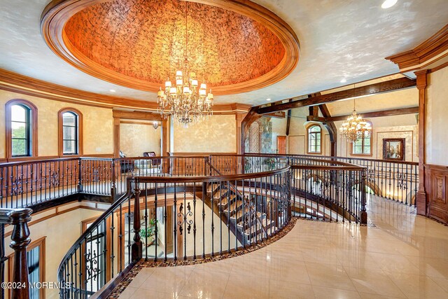 corridor featuring ornamental molding, a raised ceiling, and a notable chandelier