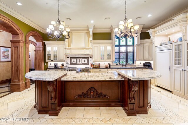 kitchen featuring light stone counters, a spacious island, custom exhaust hood, and a chandelier