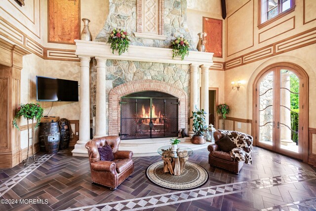 living room with a stone fireplace, a high ceiling, dark parquet flooring, and ornate columns