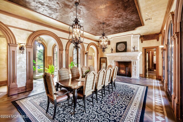 dining area featuring a raised ceiling, a high end fireplace, a notable chandelier, ornamental molding, and dark parquet floors