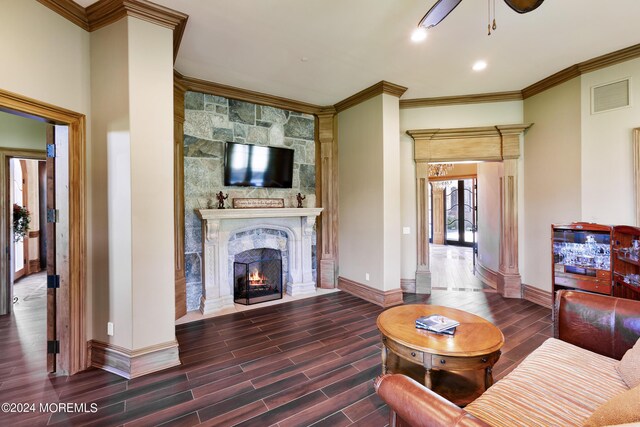 living room featuring crown molding, dark wood-type flooring, ceiling fan, and a stone fireplace