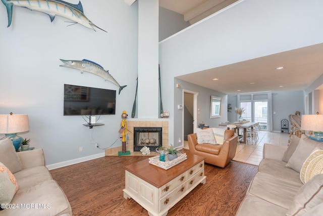 living area with baseboards, a tile fireplace, wood finished floors, a high ceiling, and recessed lighting