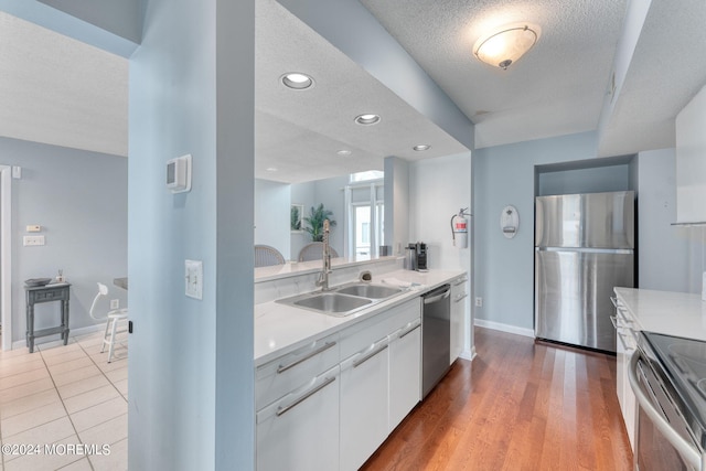 kitchen with sink, a textured ceiling, light hardwood / wood-style floors, white cabinetry, and stainless steel appliances