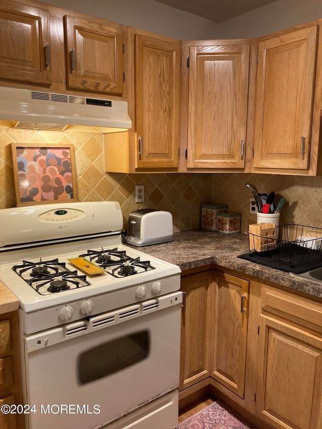 kitchen with white gas stove and tasteful backsplash