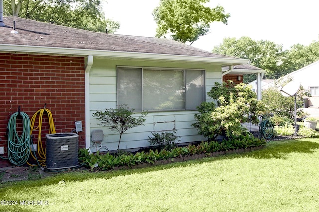 view of home's exterior with central air condition unit, roof with shingles, a lawn, and brick siding