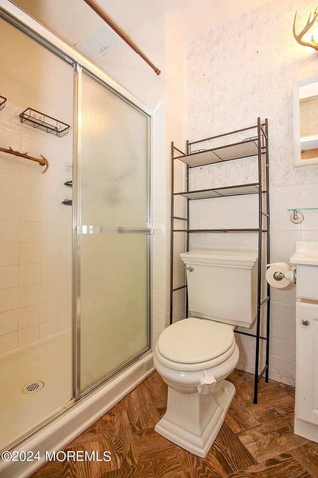 bathroom with wainscoting, toilet, vanity, a shower stall, and tile walls