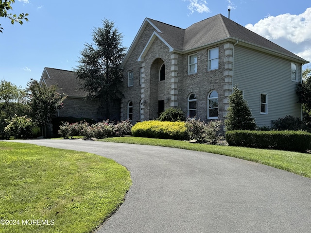 view of front of home featuring driveway, stone siding, and a front yard