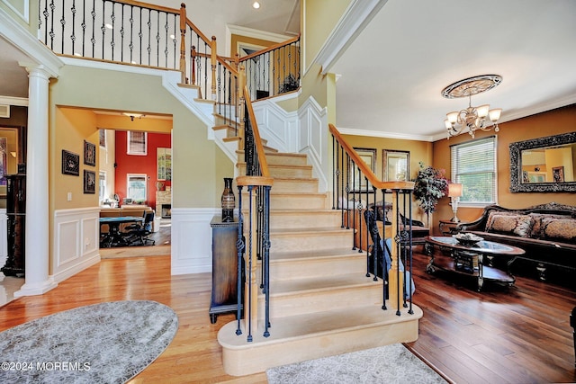 staircase featuring hardwood / wood-style flooring, a notable chandelier, wainscoting, ornate columns, and crown molding