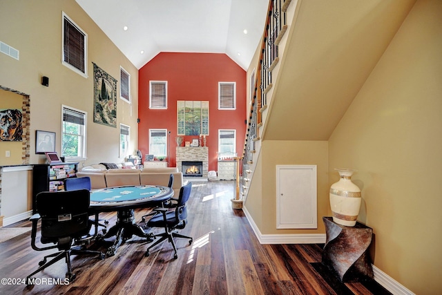 office area with baseboards, high vaulted ceiling, wood finished floors, and a stone fireplace