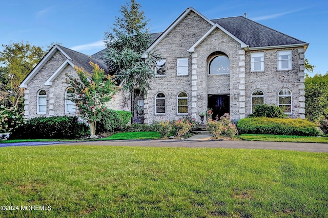 view of front of home with roof with shingles, brick siding, and a front lawn