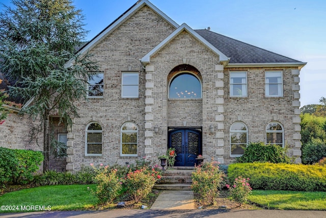 view of front of home featuring french doors, a shingled roof, and brick siding