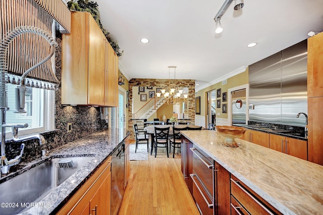 kitchen with light wood-style flooring, a sink, ornamental molding, backsplash, and dark stone counters