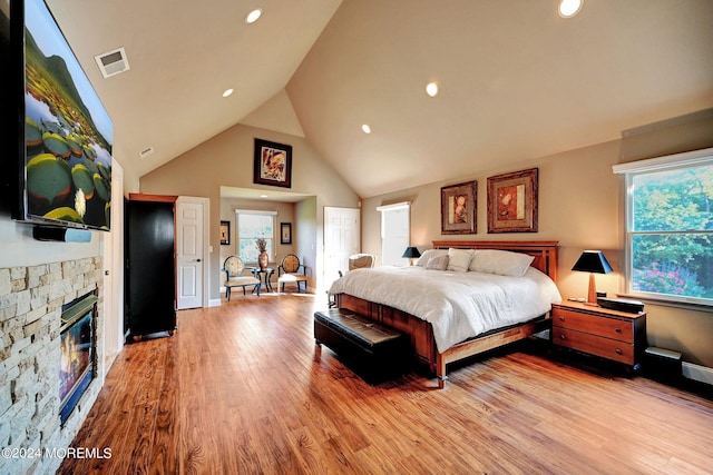 bedroom featuring light wood finished floors, multiple windows, baseboards, and a stone fireplace