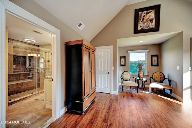 sitting room with light wood-type flooring, visible vents, vaulted ceiling, and baseboards