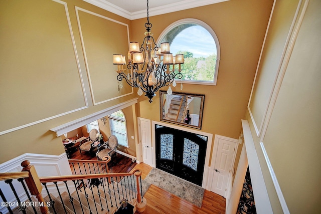 entrance foyer featuring a decorative wall, wood finished floors, stairs, an inviting chandelier, and crown molding