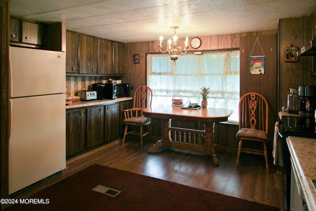 kitchen featuring a textured ceiling, wooden walls, dark hardwood / wood-style flooring, a notable chandelier, and white fridge