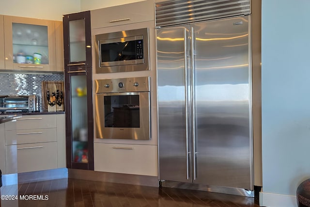 kitchen featuring a toaster, glass insert cabinets, built in appliances, dark countertops, and modern cabinets