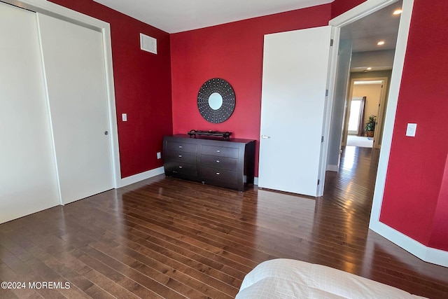 unfurnished bedroom with wood finished floors, visible vents, a closet, and baseboards