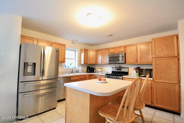 kitchen with a kitchen bar, sink, a center island, appliances with stainless steel finishes, and light tile patterned flooring