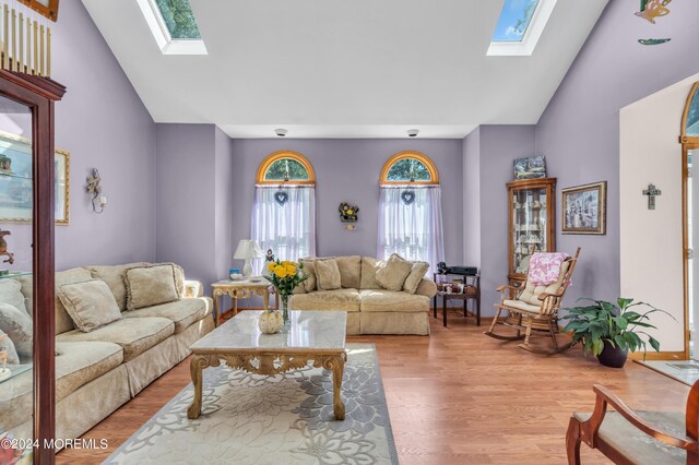 living room featuring light wood-type flooring, a skylight, and high vaulted ceiling