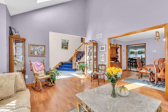 living room featuring visible vents, light wood-style flooring, a high ceiling, and stairs