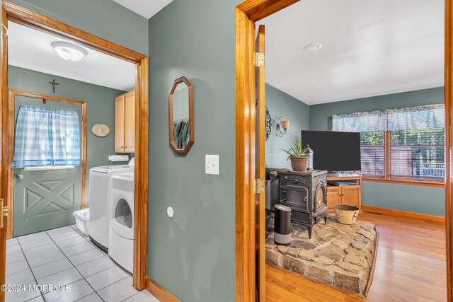 laundry room with baseboards, light wood-style floors, washer and dryer, cabinet space, and a wood stove