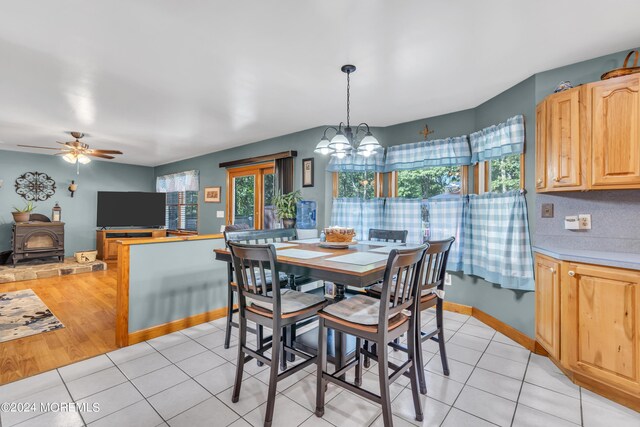 dining space with ceiling fan with notable chandelier, a wood stove, baseboards, and light tile patterned floors