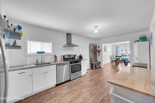 kitchen featuring stainless steel appliances, a sink, white cabinets, wall chimney range hood, and open shelves