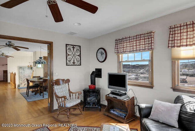 living room featuring ceiling fan, hardwood / wood-style flooring, and a wood stove