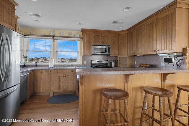 kitchen with light wood-type flooring, a kitchen breakfast bar, decorative backsplash, appliances with stainless steel finishes, and kitchen peninsula