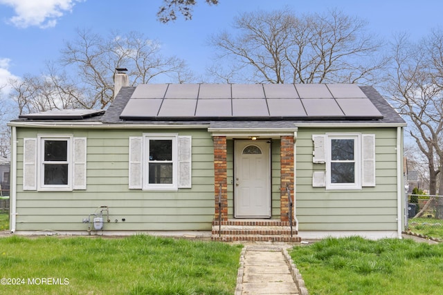 bungalow with roof mounted solar panels, a front lawn, a chimney, and a shingled roof