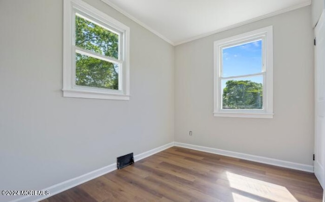 spare room with plenty of natural light, wood finished floors, baseboards, and ornamental molding