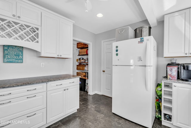 kitchen with dark stone counters, white cabinetry, ceiling fan, and white fridge