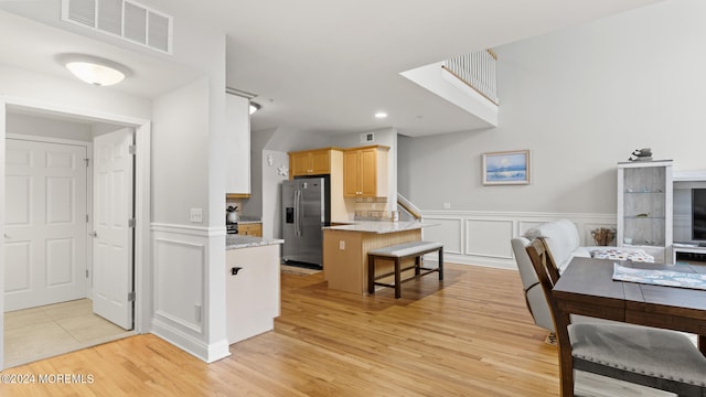 kitchen with a breakfast bar area, stainless steel fridge, light hardwood / wood-style flooring, light brown cabinetry, and light stone counters