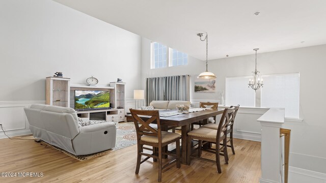 dining space with a towering ceiling, a chandelier, and light hardwood / wood-style floors