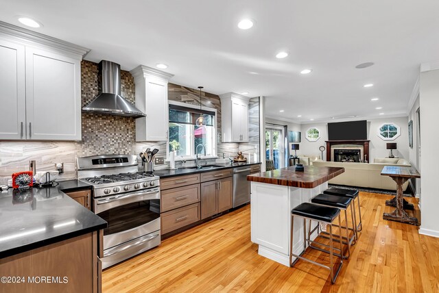 kitchen featuring wall chimney range hood, white cabinets, appliances with stainless steel finishes, and light hardwood / wood-style flooring