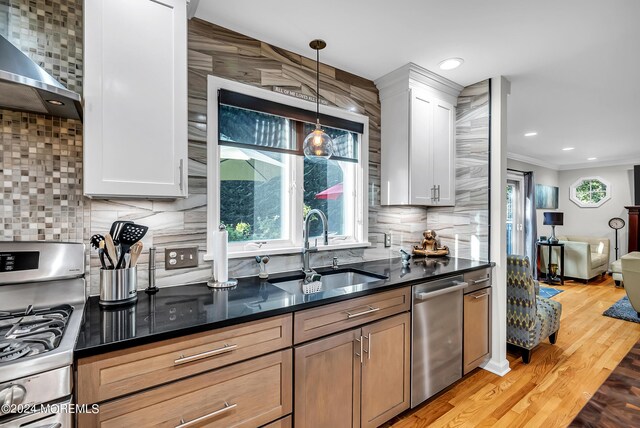 kitchen with wall chimney exhaust hood, tasteful backsplash, stainless steel appliances, sink, and light wood-type flooring