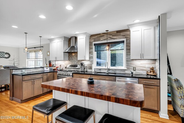 kitchen with wall chimney exhaust hood, wood counters, light hardwood / wood-style floors, tasteful backsplash, and sink