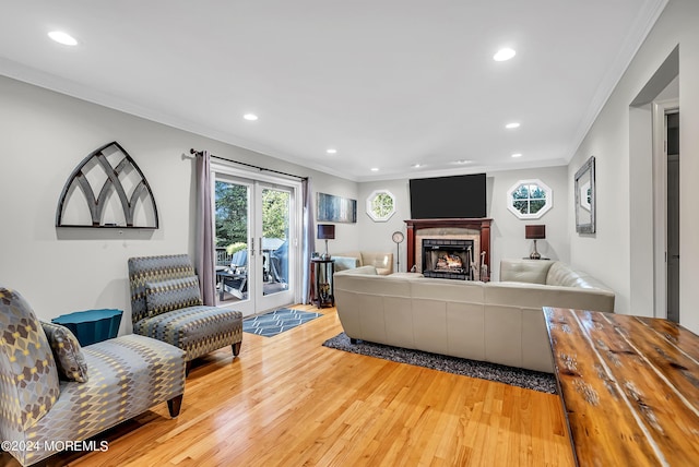 living room with a warm lit fireplace, recessed lighting, light wood-style flooring, and crown molding