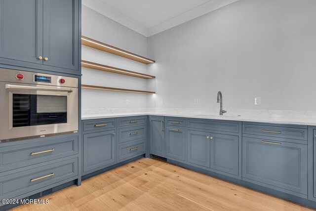 kitchen with blue cabinetry, light wood-type flooring, oven, ornamental molding, and sink