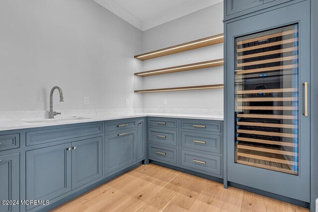 bar with wine cooler, blue cabinetry, light wood-type flooring, ornamental molding, and sink