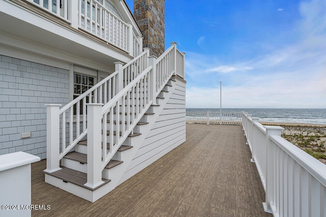 wooden terrace featuring a water view and a beach view