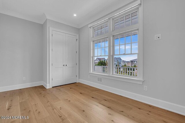 unfurnished bedroom featuring light wood-type flooring, crown molding, and a closet